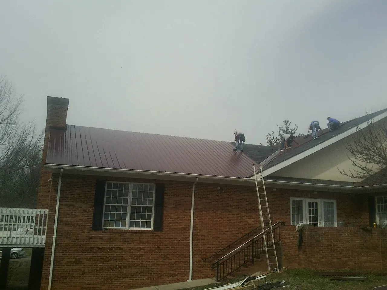 Crew setting red metal roofing panels on a brick home in Sidney